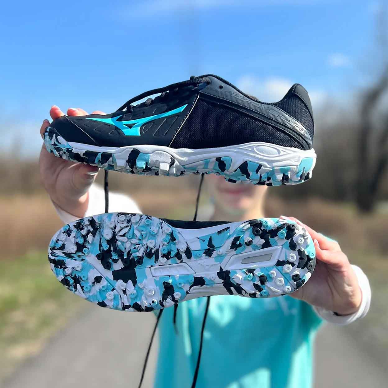 Girl holding a pair of Mizuno Wave Lynx Turf Shoes up in front of her.