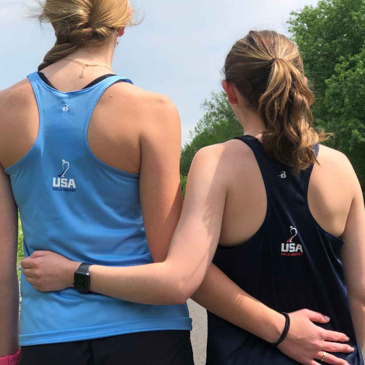 The backs of two girls wearing the USA Field Hockey Performance Tanks with their arms around each other.