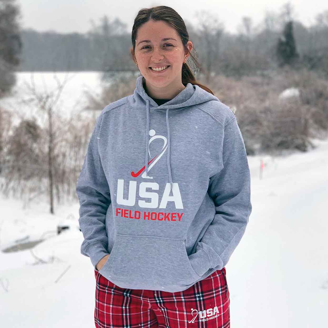 Girl wearing the grey USA Field Hockey Hooded Sweatshirt with her hands in the front pocket.