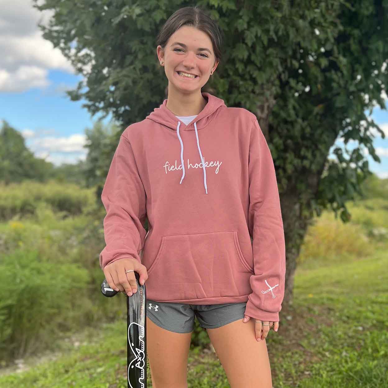 smiling girl wearing the pink Field Hockey Unisex Pullover Hooded Sweatshirt