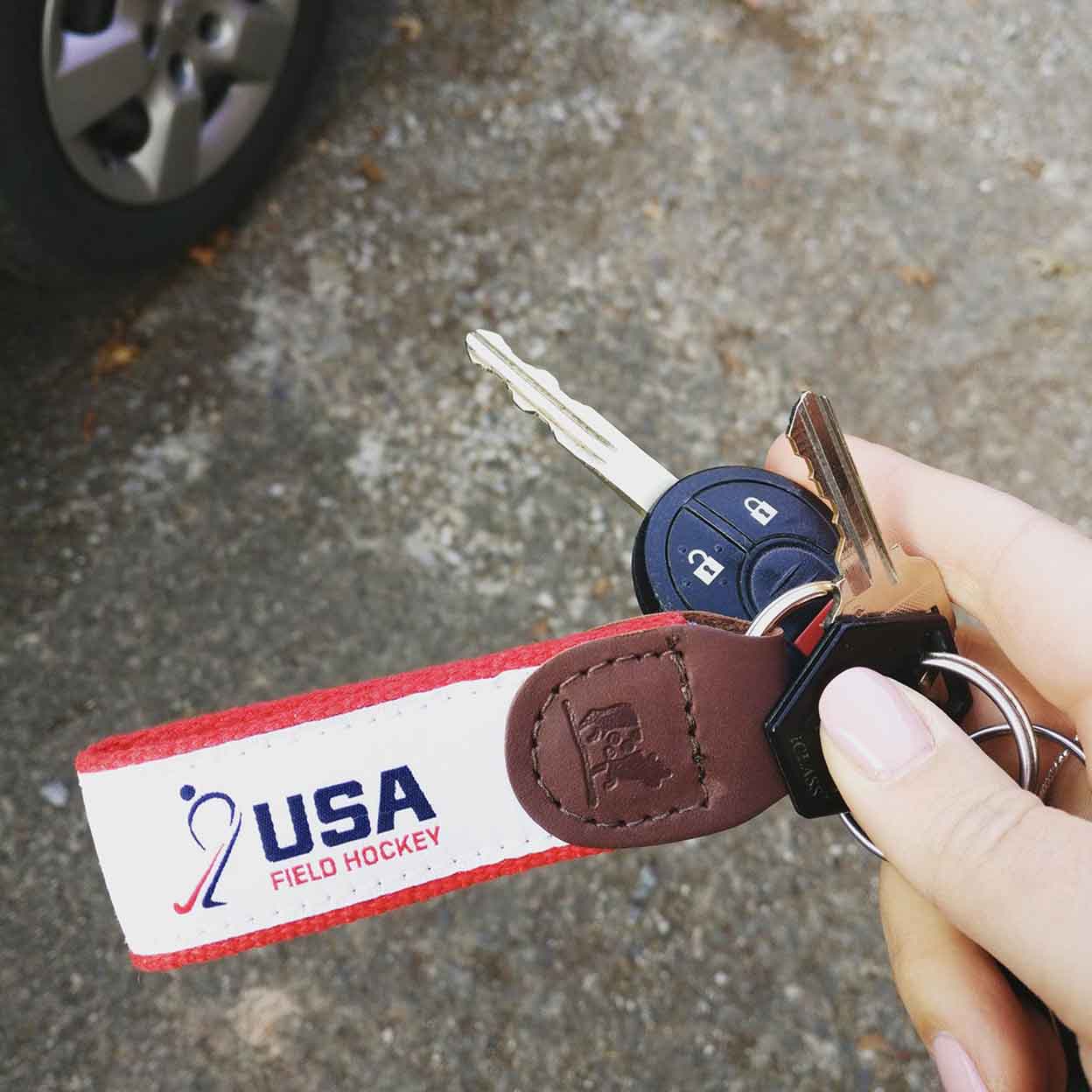 A hand holding car keys with the USA Field Hockey Ribbon Key Fob attached.