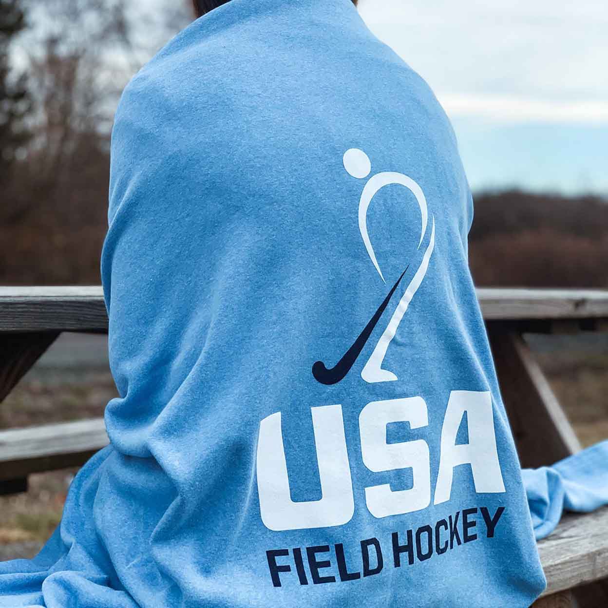 Blue USA Field Hockey Sweatshirt Blanket wrapped around the back of someone sitting on bleachers